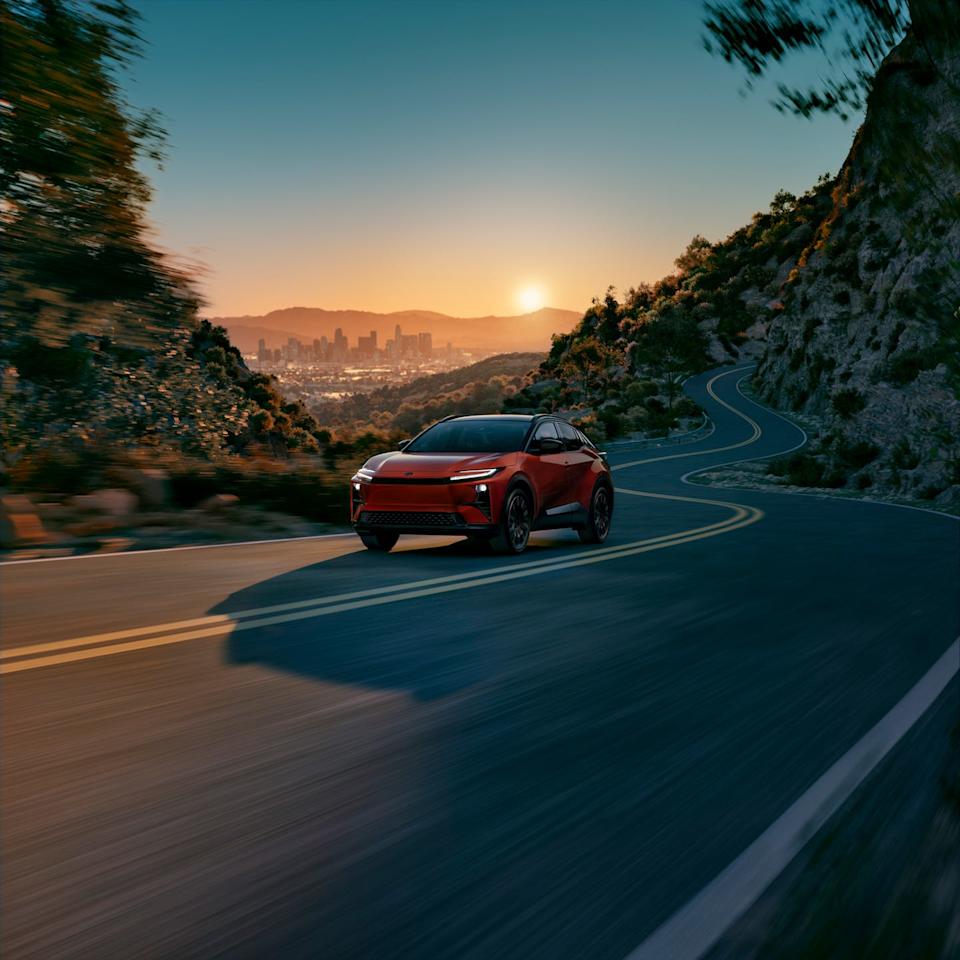 red electric suv driving on a winding mountain road at sunset with a city skyline in the background.